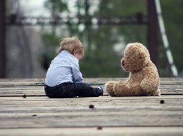 Young boy sitting beside teddy bear