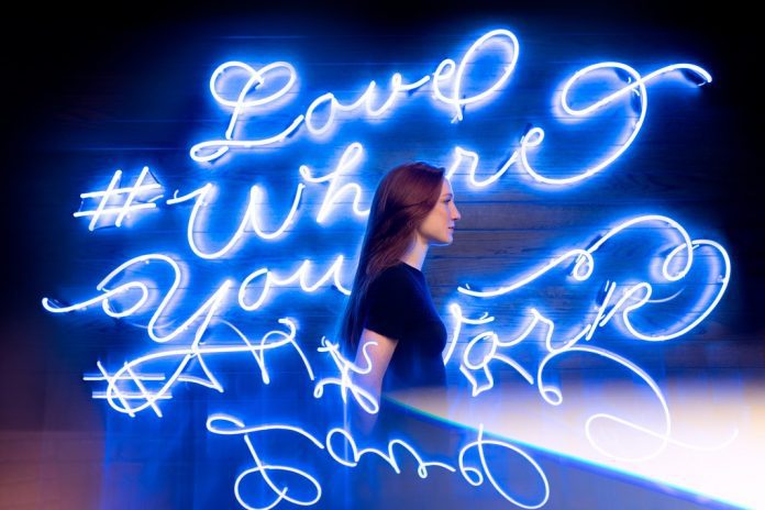 lady in front of neon blue lights that read love where you are