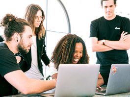 A Group of smiling Professionals huddled around laptops Sharing Ideas