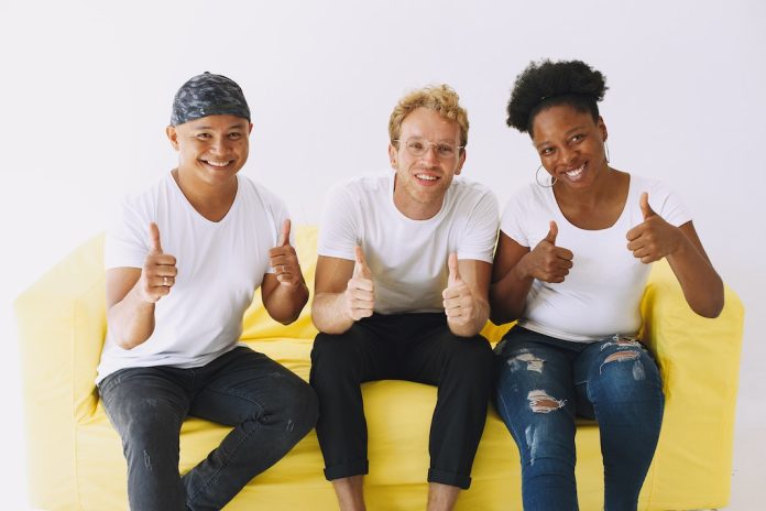 3 people sitting on yellow sofa with big smiles giving a thumbs up