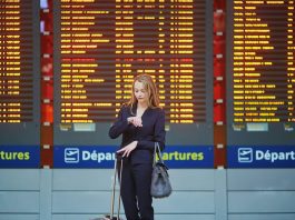 woman checking watch in airport in front of flight information