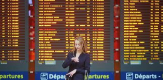 woman checking watch in airport in front of flight information
