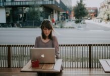 lady sitting at a table on sidewalk working on apple laptop