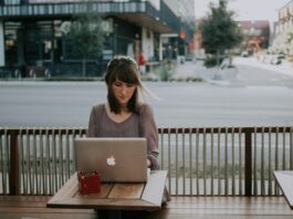lady sitting at a table on sidewalk working on apple laptop