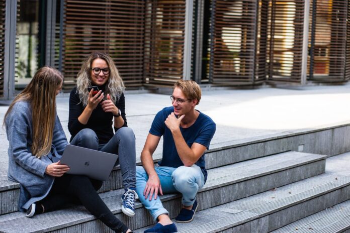 3 younger looking people sitting on steps with laptops